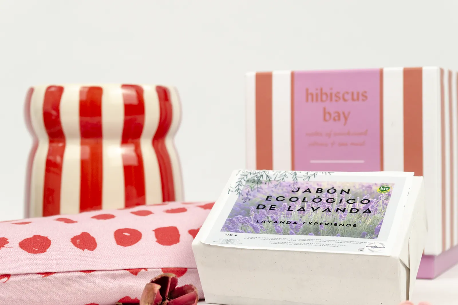 Caja de regalo de bienestar «Aromas de La Provenza» con vela Paddywax de rayas rojas y blancas, jabón de lavanda y almohada rosa con corazones rojos.