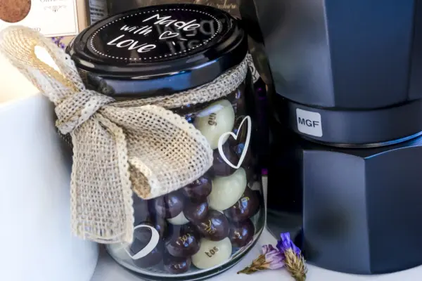 Caja regalo Musuka "Los buenos días empiezan con café" que contiene una cafetera Magefesa, una taza de cerámica artesanal en la que se lee "good days start with coffe", un paquete de galletas de cacao Lady Joseph, un paquete de Café Molido Bio “Tierra Madre Mujer”, de Oxfam Intermón Comercio Justo y un tarro de cacahuetes recubiertos de chocolate blanco y negro.