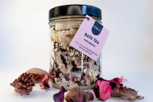 Caja de regalo Musuka "Mímate" que contiene: Una vela con olor a higuera silvestre y cedro, una herramienta para velas, un tarro de sales de baño con aroma a hibisco y rosa, un rodillo de masaje facial que se convierte en bolígrafo y una botella “Paddywax” con cerillas.
