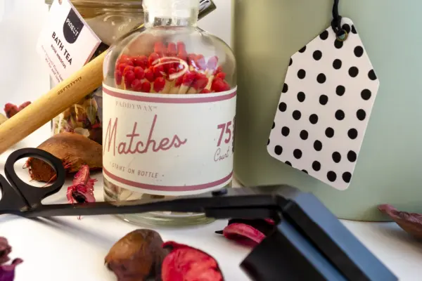 Caja de regalo Musuka "Mímate" que contiene: Una vela con olor a higuera silvestre y cedro, una herramienta para velas, un tarro de sales de baño con aroma a hibisco y rosa, un rodillo de masaje facial que se convierte en bolígrafo y una botella “Paddywax” con cerillas.