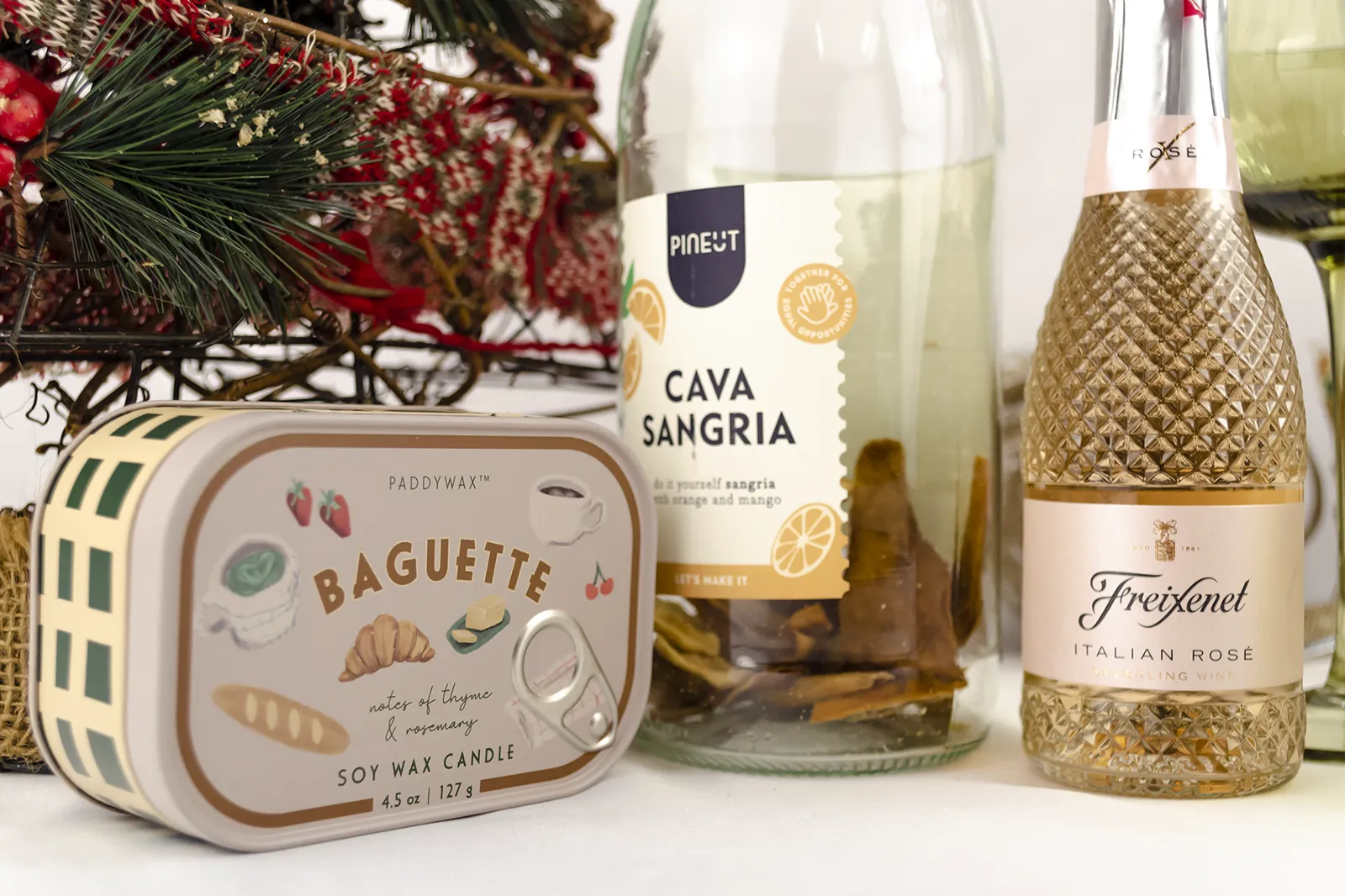 Caja Musuka “Regalo de Navidad 11" que contiene: Una botella de sangría de cava Pineut, con una mezcla de naranja y mango deshidratados. Una mini botella de vino Freixenet "Italian Rosé” de 20 cl. Una vela enlatada Paddywax “Baguette".