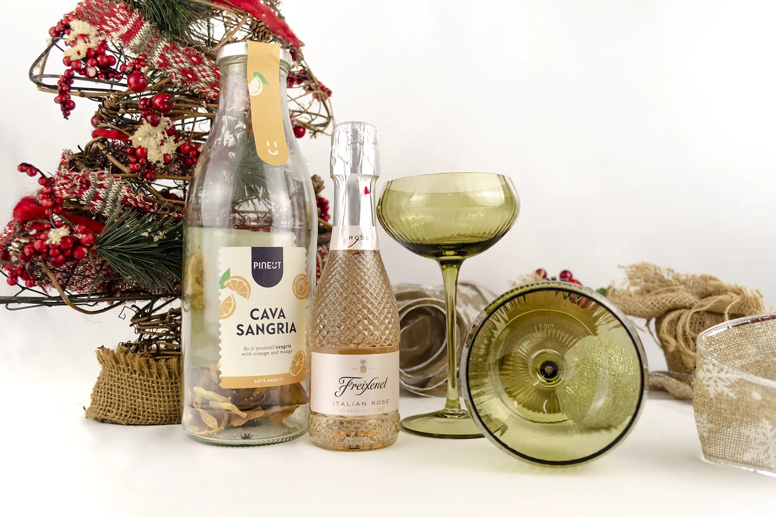 Caja Musuka “Regalo de Navidad 16" que contiene: dos copas estilo vintage “Here’s How”, de color verde. Una botella de sangría de cava Pineut. Contiene una mezcla de naranja y mango deshidratados, para preparar tu propia sangría. Una mini botella de vino Freixenet "Italian Rosé” de 20 cl.