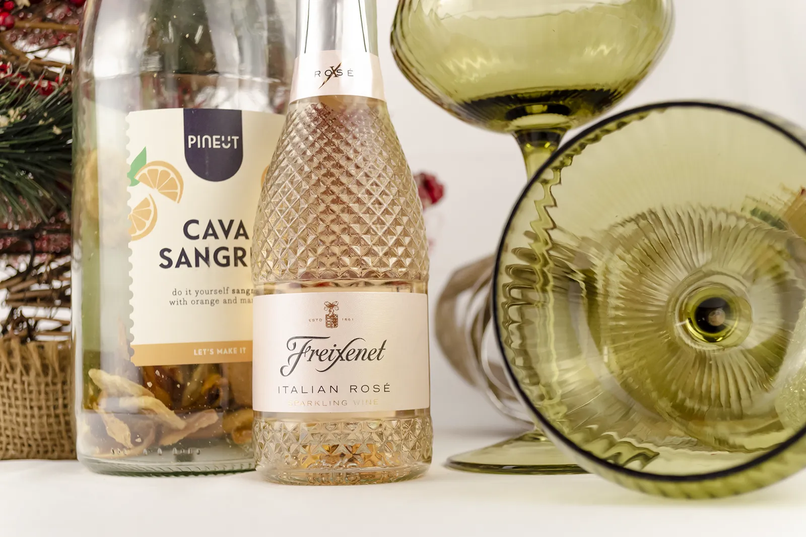 Caja Musuka “Regalo de Navidad 16" que contiene: dos copas estilo vintage “Here’s How”, de color verde. Una botella de sangría de cava Pineut. Contiene una mezcla de naranja y mango deshidratados, para preparar tu propia sangría. Una mini botella de vino Freixenet "Italian Rosé” de 20 cl.