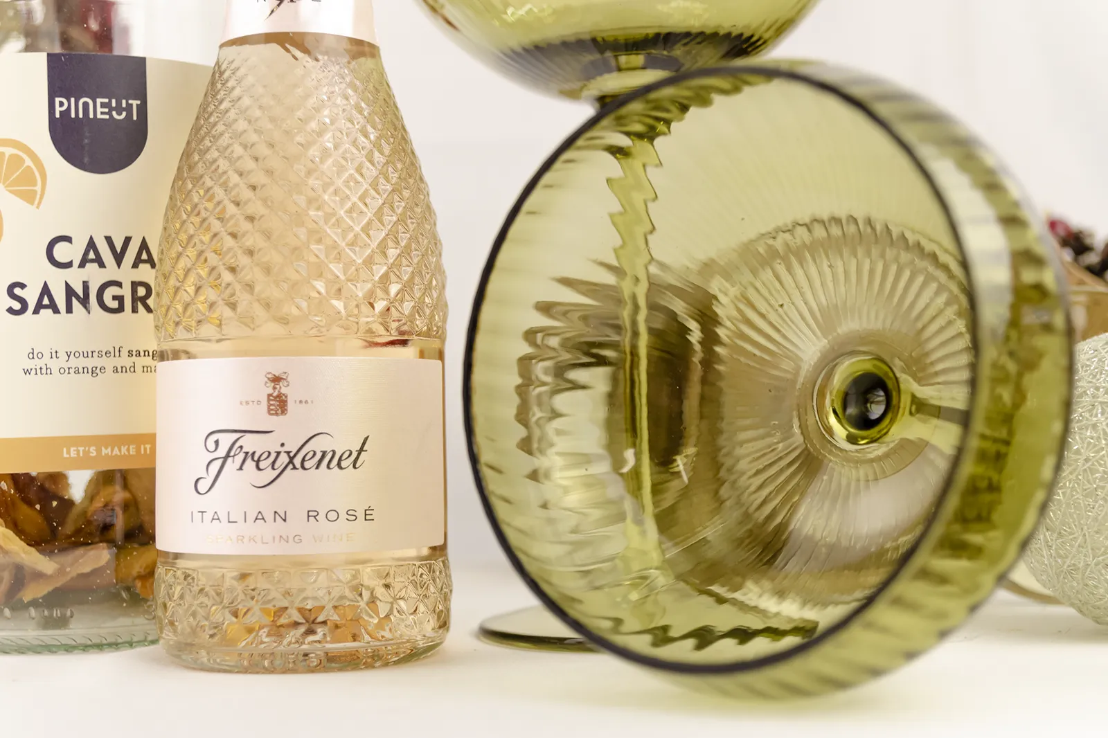 Caja Musuka “Regalo de Navidad 16" que contiene: dos copas estilo vintage “Here’s How”, de color verde. Una botella de sangría de cava Pineut. Contiene una mezcla de naranja y mango deshidratados, para preparar tu propia sangría. Una mini botella de vino Freixenet "Italian Rosé” de 20 cl.