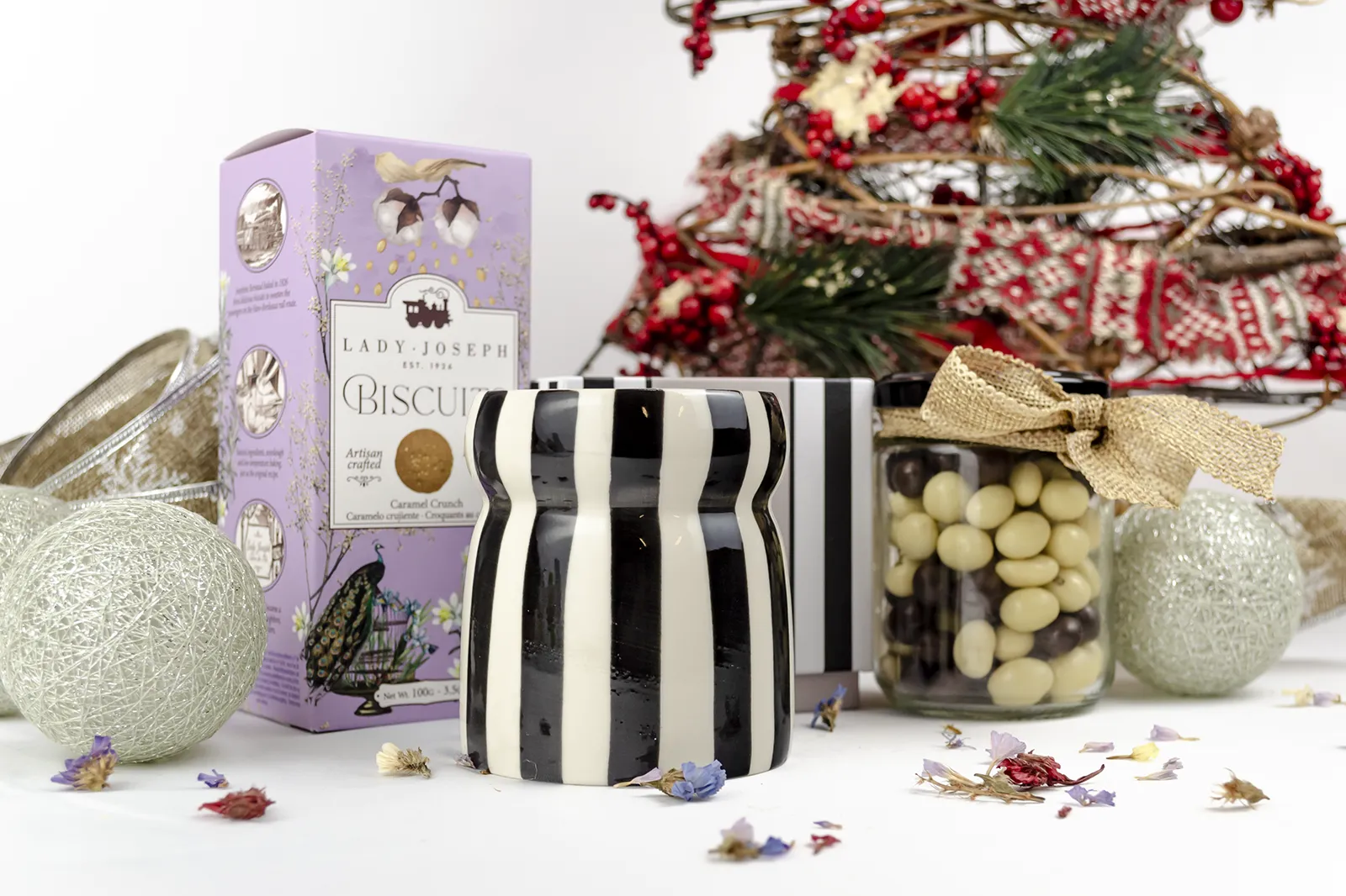 Caja Musuka “Regalo de Navidad 19" que contiene: Una vela Paddywax “Lava Stone”, en un vaso de rayas negras y blancas. Un paquete de galletas de caramelo crujiente Lady Joseph. Un tarro de cacahuetes recubiertos de chocolate blanco y negro.