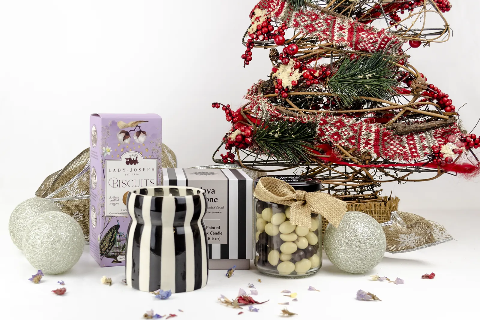 Caja Musuka “Regalo de Navidad 19" que contiene: Una vela Paddywax “Lava Stone”, en un vaso de rayas negras y blancas. Un paquete de galletas de caramelo crujiente Lady Joseph. Un tarro de cacahuetes recubiertos de chocolate blanco y negro.