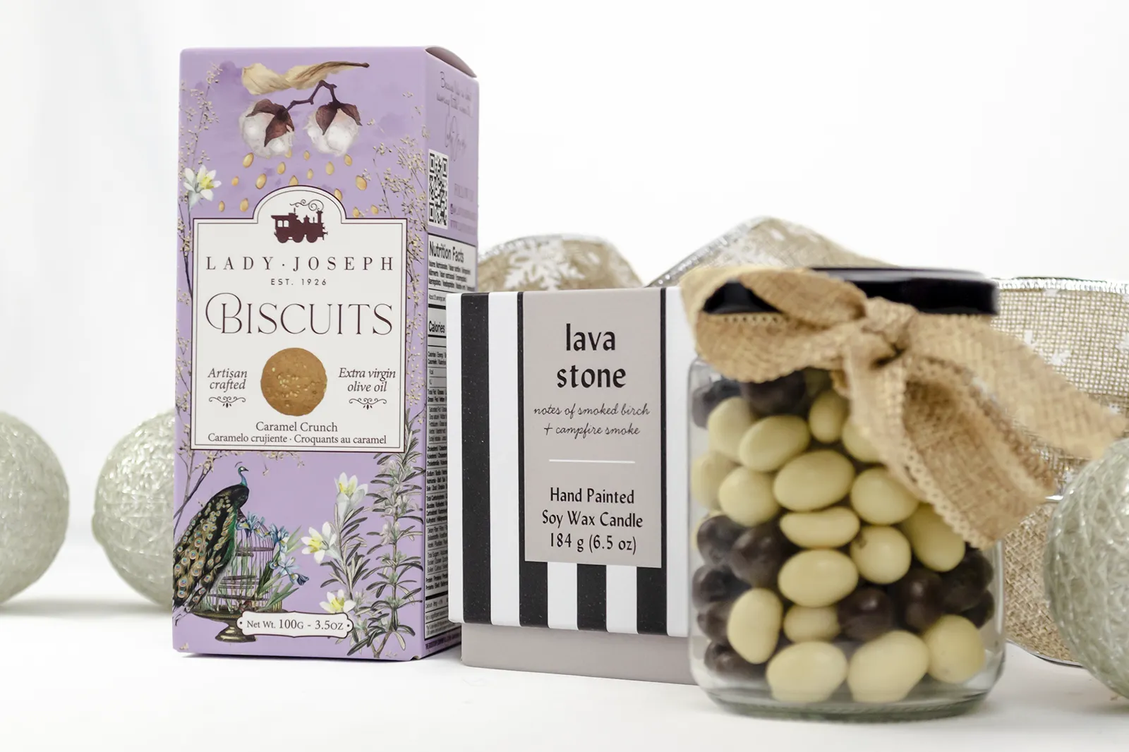 Caja Musuka “Regalo de Navidad 19" que contiene: Una vela Paddywax “Lava Stone”, en un vaso de rayas negras y blancas. Un paquete de galletas de caramelo crujiente Lady Joseph. Un tarro de cacahuetes recubiertos de chocolate blanco y negro.