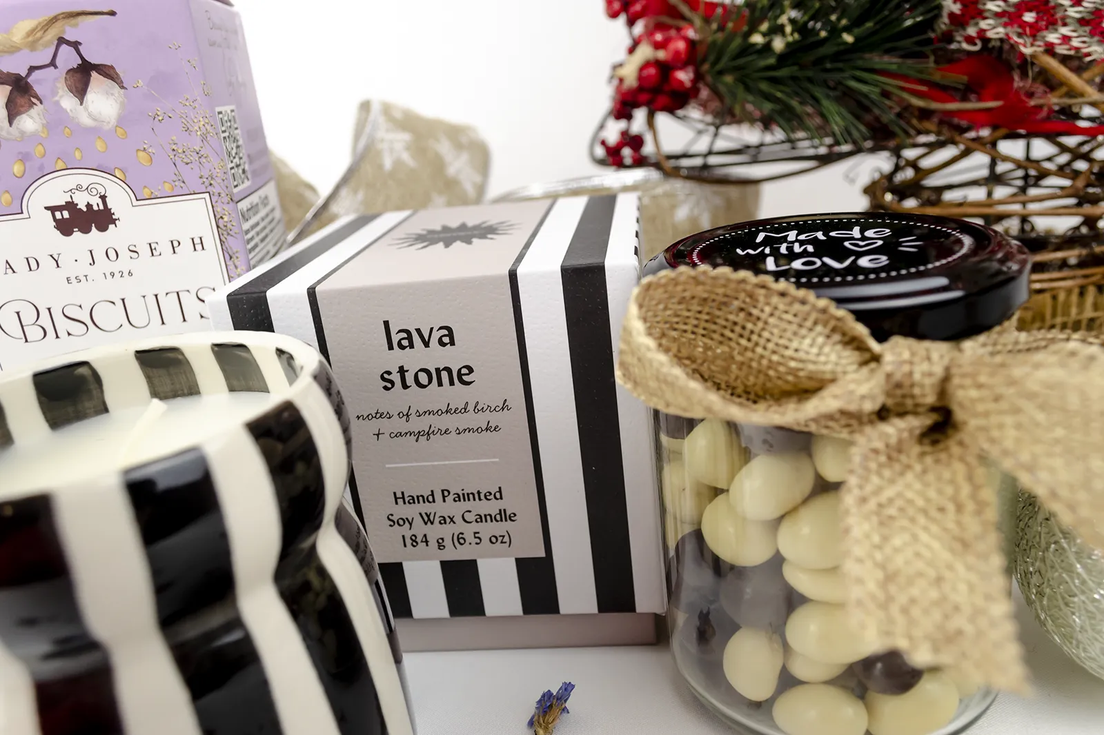 Caja Musuka “Regalo de Navidad 19" que contiene: Una vela Paddywax “Lava Stone”, en un vaso de rayas negras y blancas. Un paquete de galletas de caramelo crujiente Lady Joseph. Un tarro de cacahuetes recubiertos de chocolate blanco y negro.