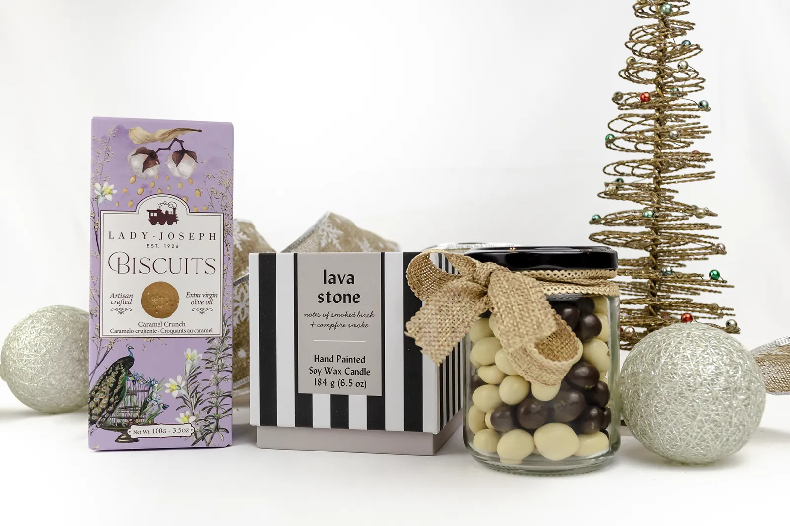 Caja Musuka “Regalo de Navidad 19" que contiene: Una vela Paddywax “Lava Stone”, en un vaso de rayas negras y blancas. Un paquete de galletas de caramelo crujiente Lady Joseph. Un tarro de cacahuetes recubiertos de chocolate blanco y negro.