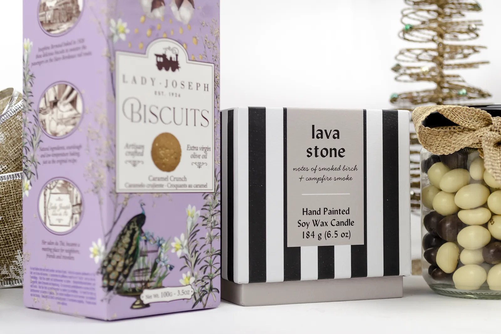 Caja Musuka “Regalo de Navidad 19" que contiene: Una vela Paddywax “Lava Stone”, en un vaso de rayas negras y blancas. Un paquete de galletas de caramelo crujiente Lady Joseph. Un tarro de cacahuetes recubiertos de chocolate blanco y negro.