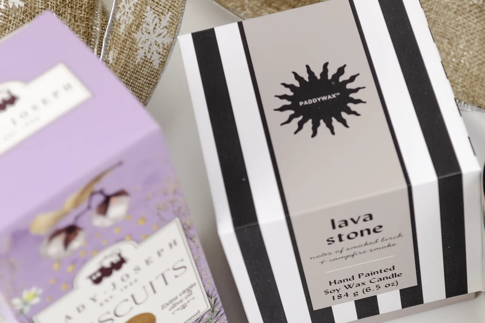 Caja Musuka “Regalo de Navidad 19" que contiene: Una vela Paddywax “Lava Stone”, en un vaso de rayas negras y blancas. Un paquete de galletas de caramelo crujiente Lady Joseph. Un tarro de cacahuetes recubiertos de chocolate blanco y negro.