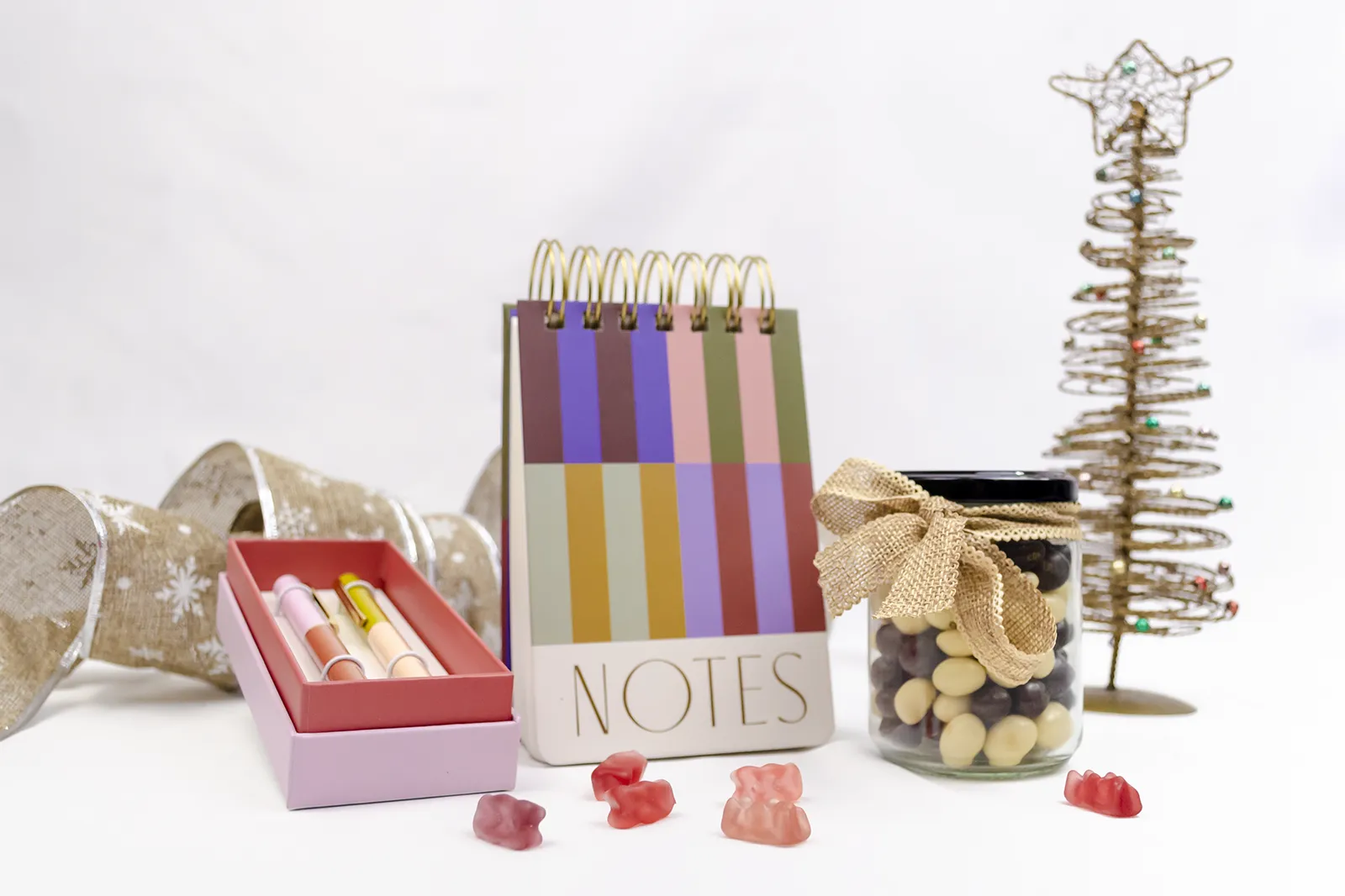 Caja Musuka “Regalo de Navidad 2" que contiene: set de bolígrafos Designworks Ink, cacahuetes cubiertos de chocolate, bloc de notas con rayas de colores.