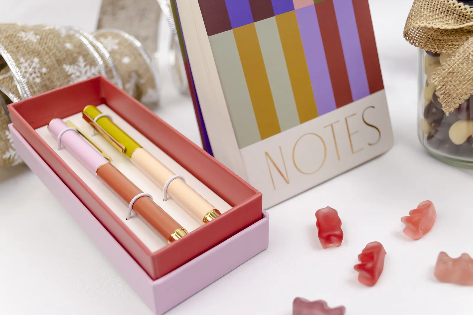 Caja Musuka “Regalo de Navidad 2" que contiene: set de bolígrafos Designworks Ink, cacahuetes cubiertos de chocolate, bloc de notas con rayas de colores.