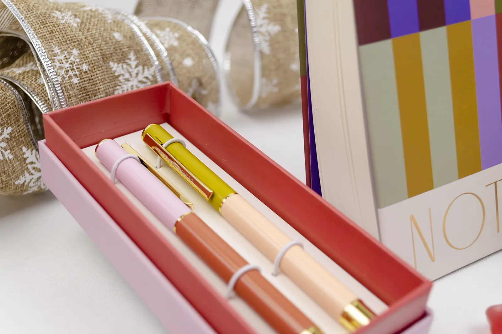 Caja Musuka “Regalo de Navidad 2" que contiene: set de bolígrafos Designworks Ink, cacahuetes cubiertos de chocolate, bloc de notas con rayas de colores.