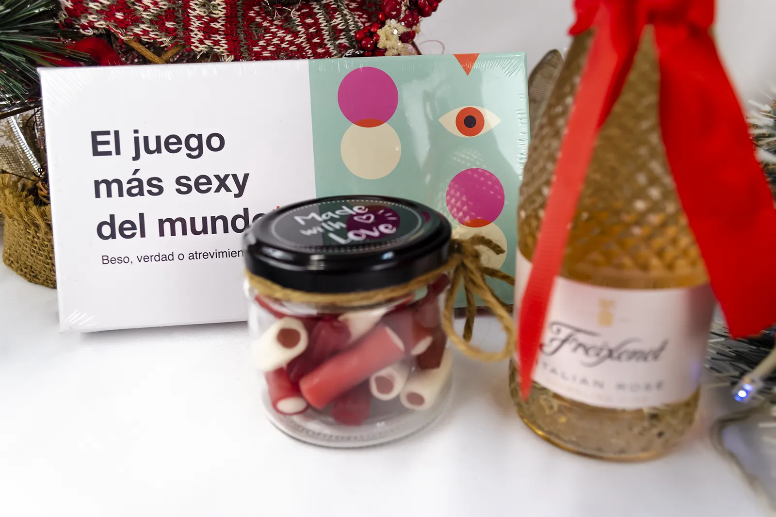Caja Musuka “Regalo de Navidad 4" que contiene: botella de vino Freixenet "Italian Rosé”, “El juego más sexy del mundo: beso, verdad o atrevimiento”. Un tarro de cristal con deliciosas gominolas rojas.