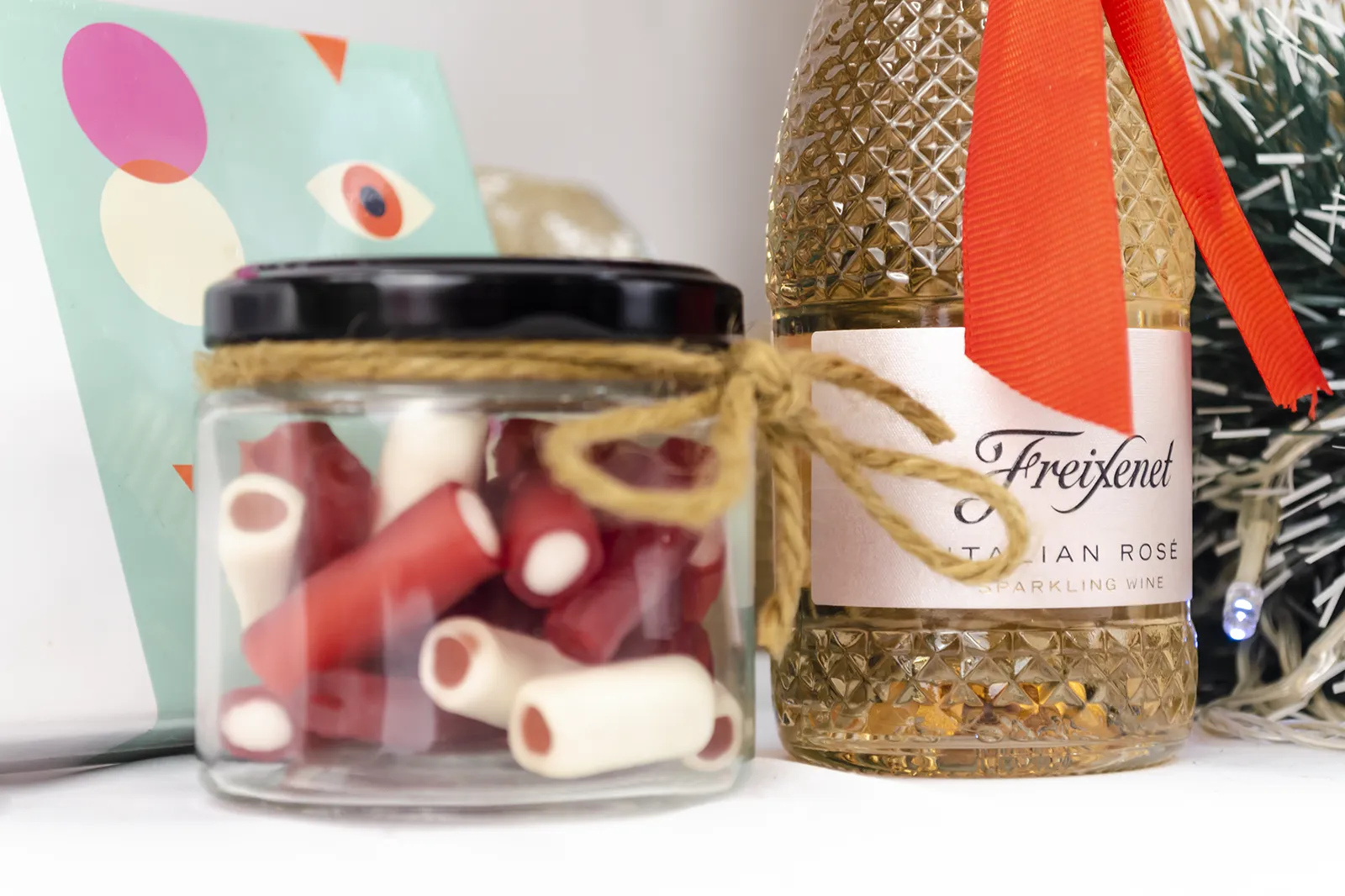 Caja Musuka “Regalo de Navidad 4" que contiene: botella de vino Freixenet "Italian Rosé”, “El juego más sexy del mundo: beso, verdad o atrevimiento”. Un tarro de cristal con deliciosas gominolas rojas.