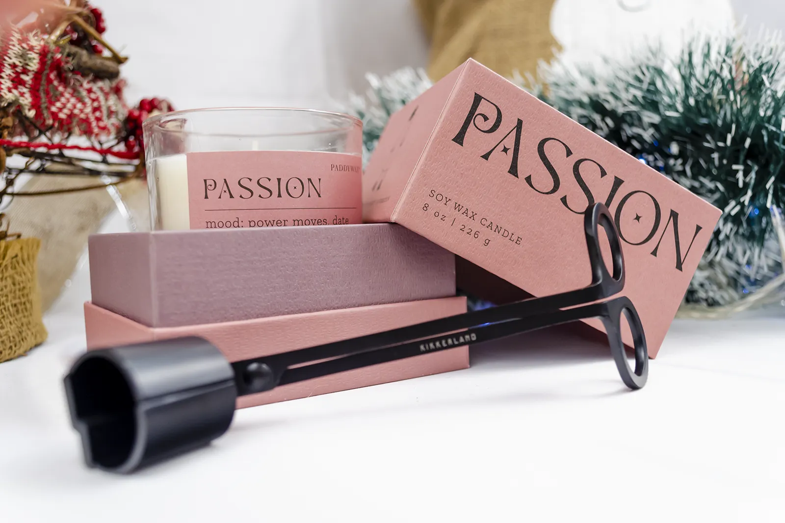 Caja Musuka “Regalo de Navidad 5" que contiene: Una vela Paddywax “Passion”, en un vaso de vidrio trasparente con borde de color rosa. Una herramienta para velas Kikkerland tres en uno.