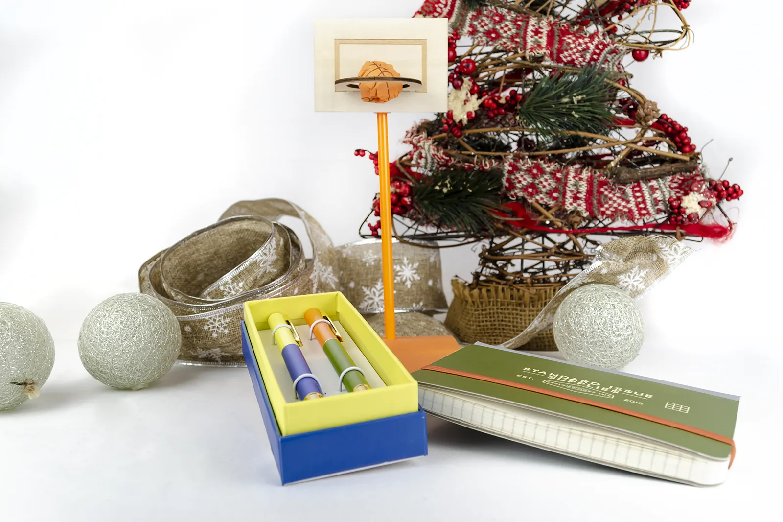 Caja Musuka “Regalo de Navidad 6" que contiene: set Kikkerland con un bloc de notas y un lápiz, con los que puedes montar una canasta. Un set de dos bolígrafos Designworks Ink, en tonos verdes y naranjas. Un cuaderno de bolsillo de tapa dura Designworks Ink con forma de pasaporte.