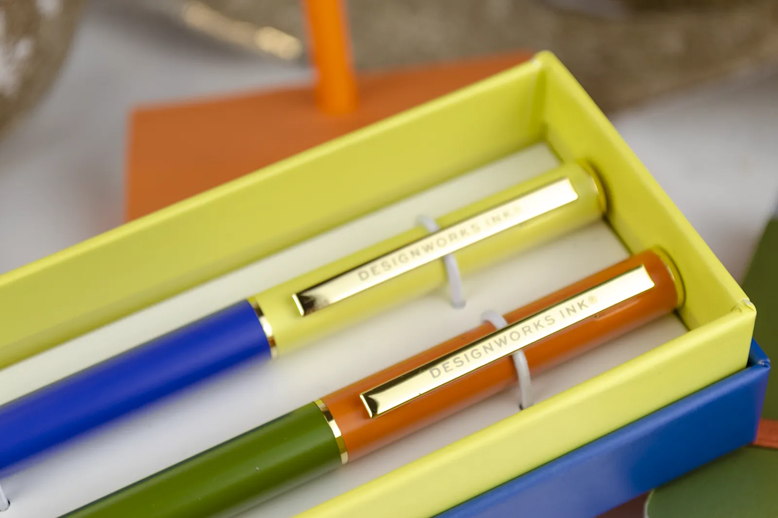 Caja Musuka “Regalo de Navidad 6" que contiene: set Kikkerland con un bloc de notas y un lápiz, con los que puedes montar una canasta. Un set de dos bolígrafos Designworks Ink, en tonos verdes y naranjas. Un cuaderno de bolsillo de tapa dura Designworks Ink con forma de pasaporte.