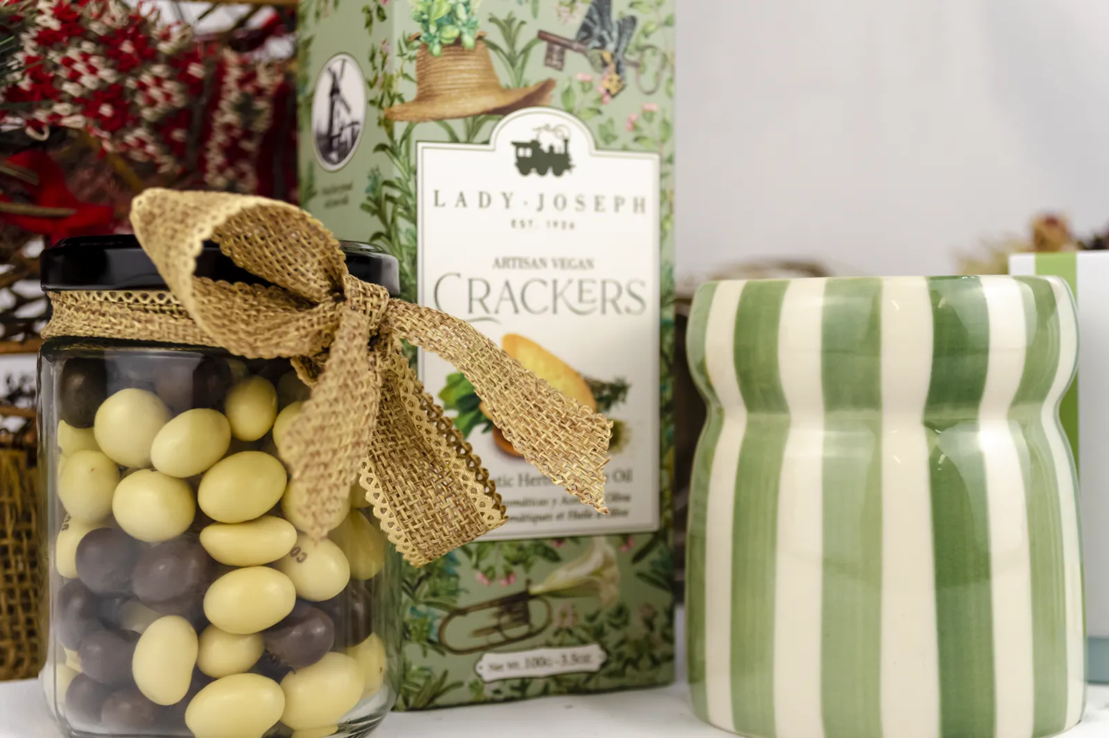 Caja Musuka “Regalo de Navidad 7" que contiene: crackers veganos Lady Joseph, vela Paddywax en un vaso de rayas verdes y blancas. Un tarro de cacahuetes recubiertos de chocolate blanco y negro.