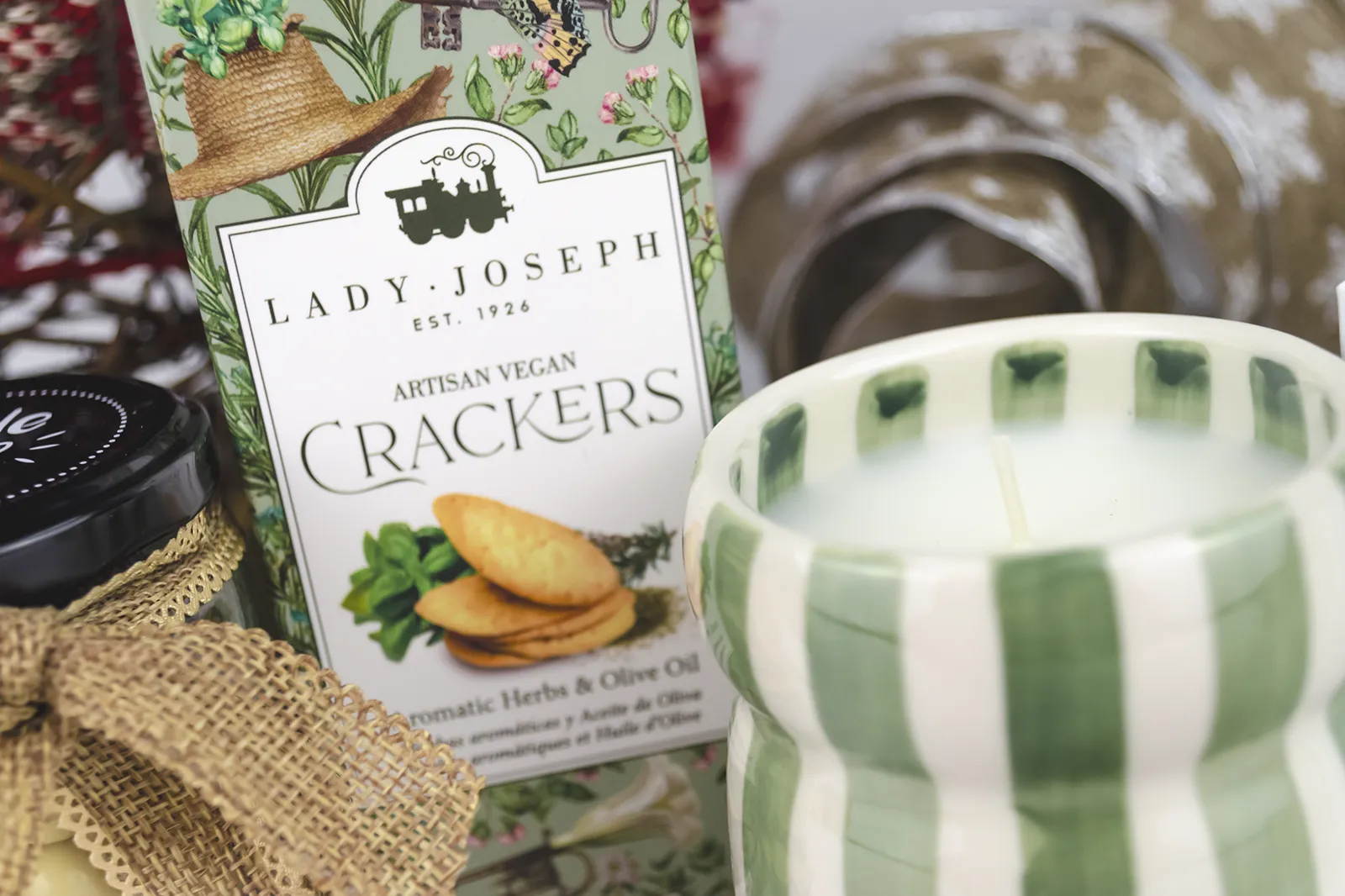 Caja Musuka “Regalo de Navidad 7" que contiene: crackers veganos Lady Joseph, vela Paddywax en un vaso de rayas verdes y blancas. Un tarro de cacahuetes recubiertos de chocolate blanco y negro.