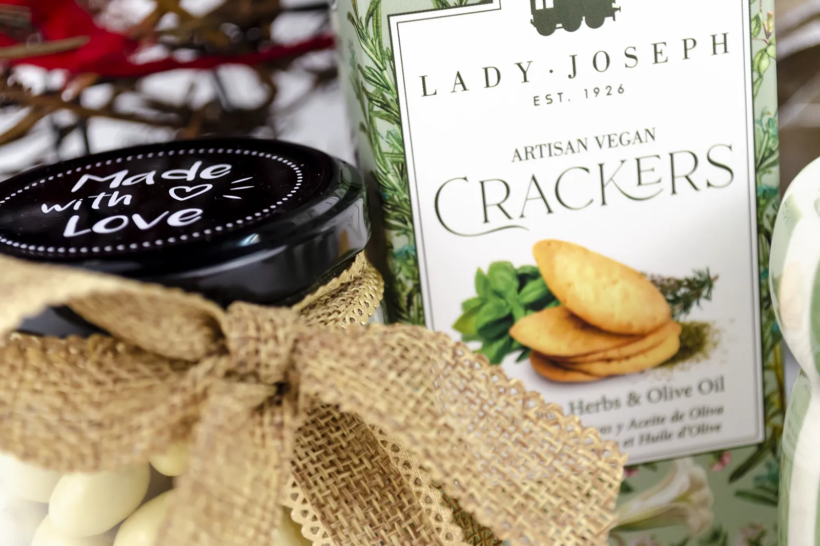 Caja Musuka “Regalo de Navidad 7" que contiene: crackers veganos Lady Joseph, vela Paddywax en un vaso de rayas verdes y blancas. Un tarro de cacahuetes recubiertos de chocolate blanco y negro.