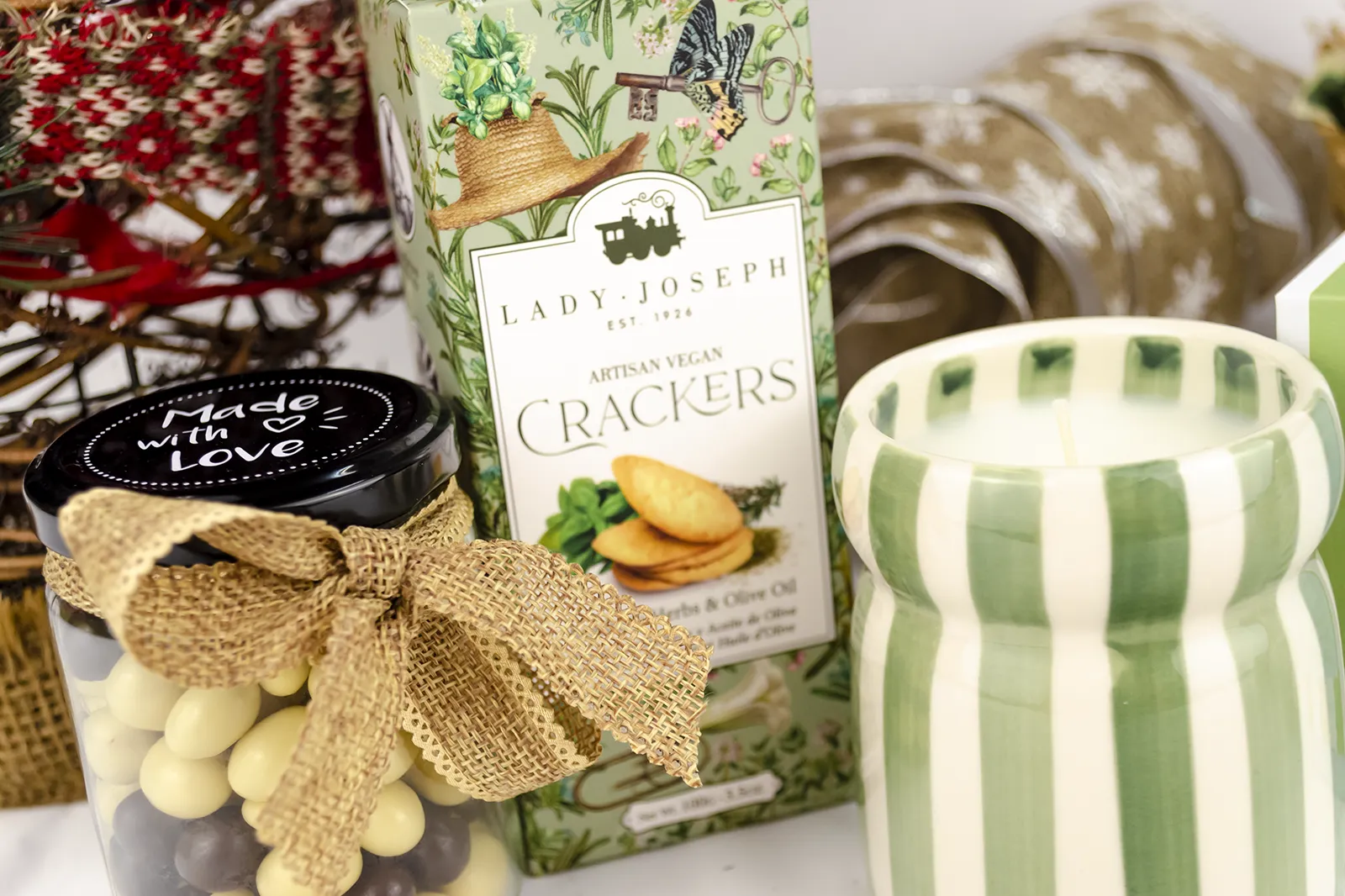 Caja Musuka “Regalo de Navidad 7" que contiene: crackers veganos Lady Joseph, vela Paddywax en un vaso de rayas verdes y blancas. Un tarro de cacahuetes recubiertos de chocolate blanco y negro.
