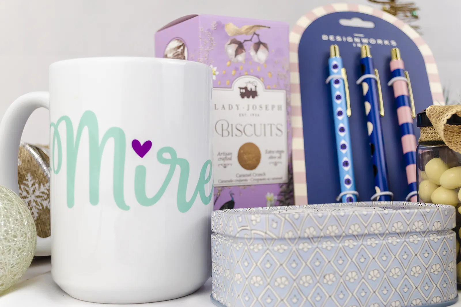 Caja Musuka “Regalo de Navidad 8" que contiene: galletas de caramelo crujiente Lady Joseph, tres bolígrafos Designworks Ink, con diferentes estampados, Una vela en lata Paddywax “Lavender Thyme” y una taza blanca personalizada.