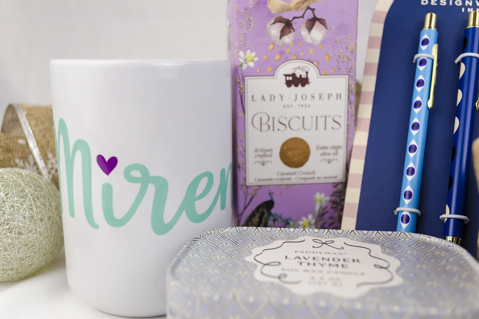 Caja Musuka “Regalo de Navidad 8" que contiene: galletas de caramelo crujiente Lady Joseph, tres bolígrafos Designworks Ink, con diferentes estampados, Una vela en lata Paddywax “Lavender Thyme” y una taza blanca personalizada.