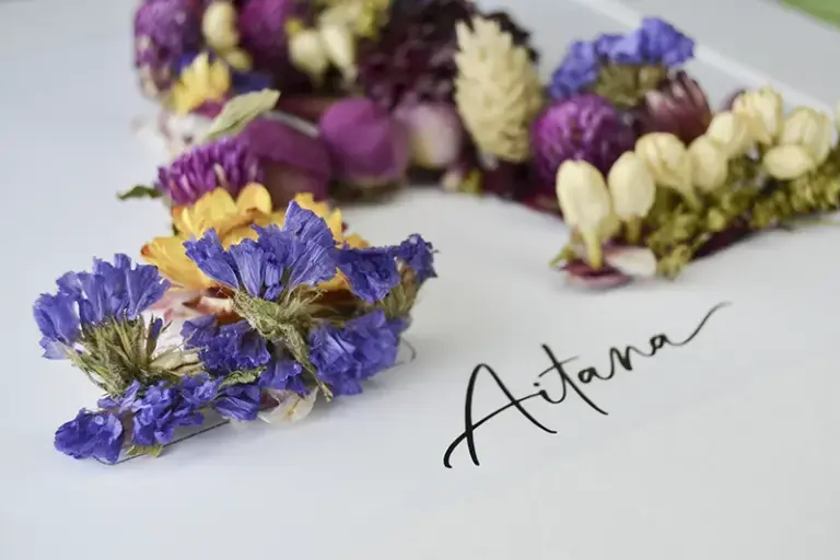 Regalo personalizado con cuadro de flores preservadas con la inicial A y nombre Aitana junto a una cesta de esparto
