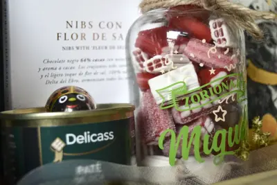 Detalle de botella de cristal personalizada con «Felicidades Miguel» junto a paté de oca y chocolate artesanal