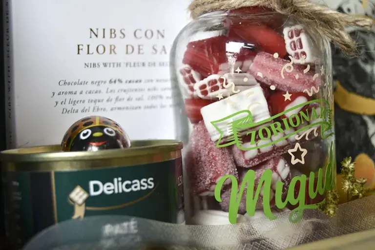 Detalle de botella de cristal personalizada con «Felicidades Miguel» junto a paté de oca y chocolate artesanal