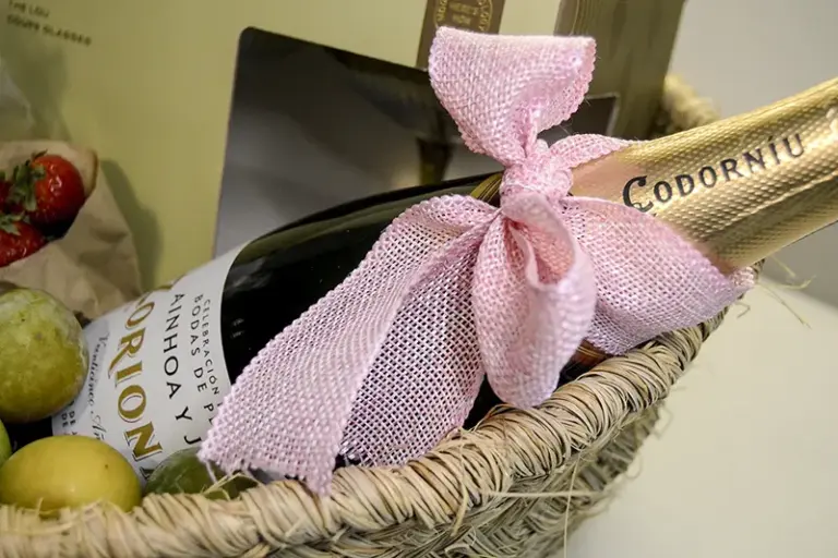 Botella de cava personalizada con lazo rosa, frutas y copas en cesta de regalo para bodas de plata