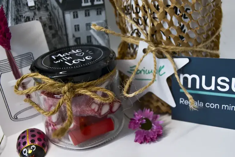 Tarro de cristal personalizado con la frase «Hecho con amor» y gominolas junto a taza personalizada envuelta y adorno de felicidades