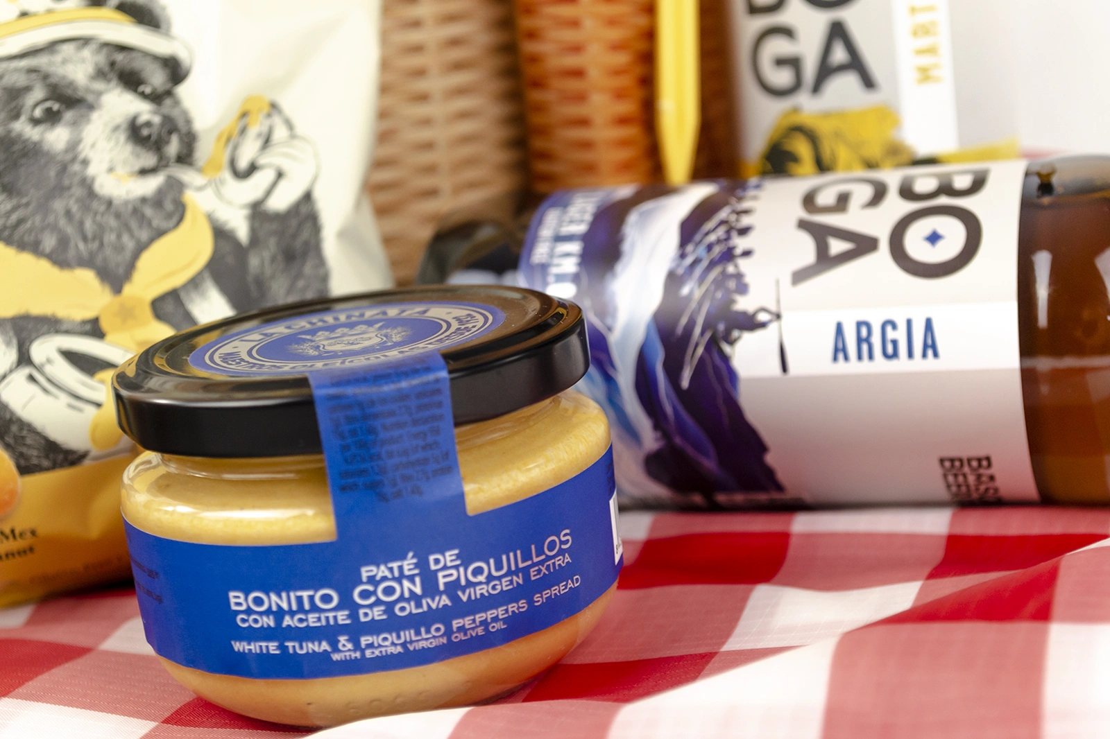 Aperitivo para pícnic con paté, cervezas Boga y snacks salados sobre un mantel de picnic, una propuesta de regalo para disfrutar de una comida al aire libre con amigos.